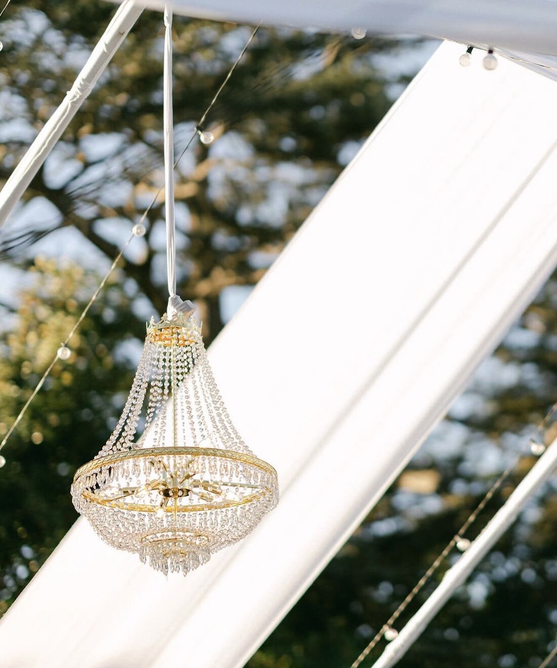 Crystal empire chandelier hung from a tented ceiling at golden hour