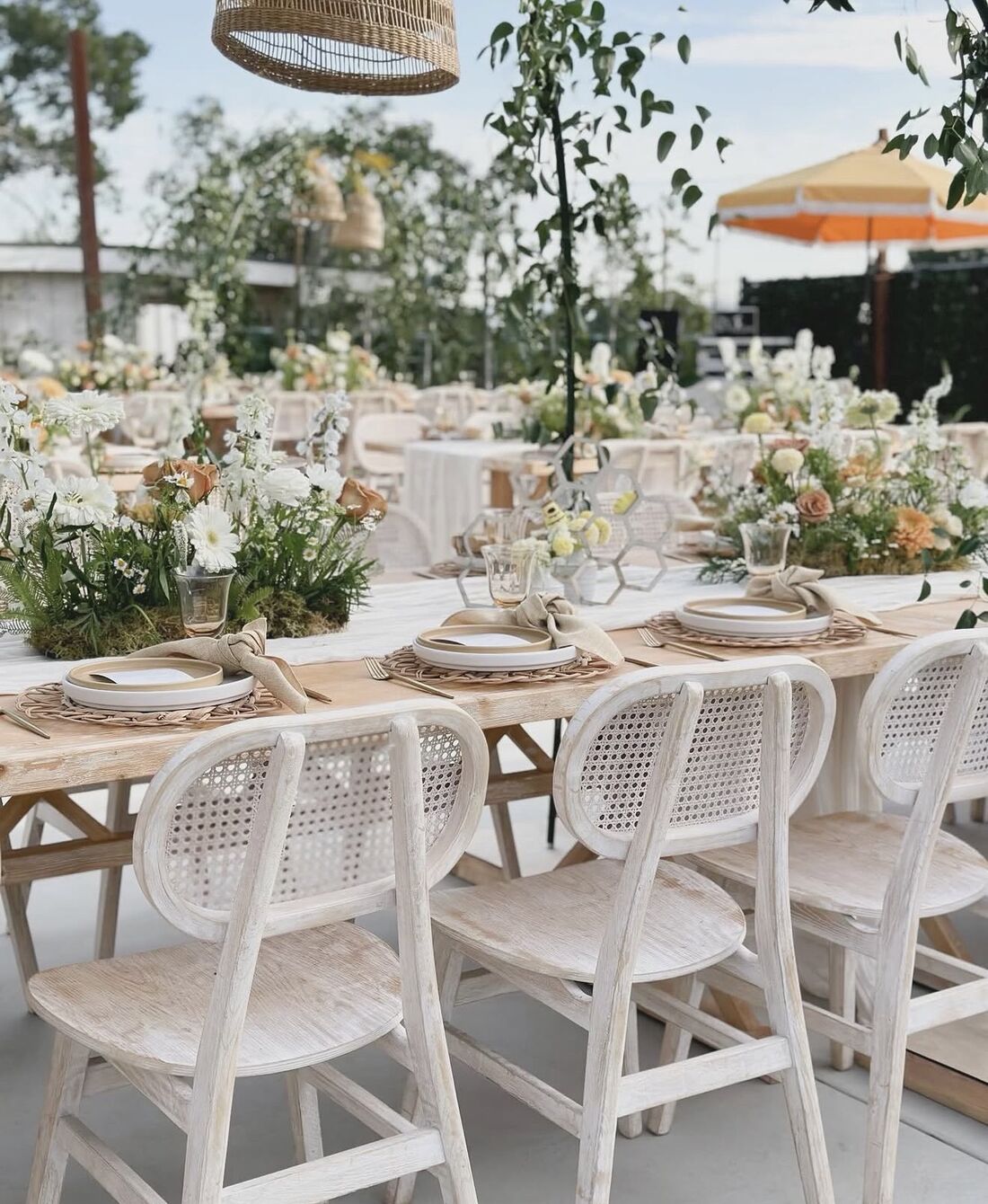 Whitewashed cane chairs and wildflower centerpieces at an outdoor garden reception